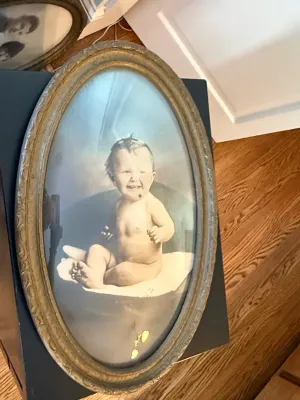 Sale Photo Thumbnail #377: Antique oval framed portrait of a seated baby set under bubble glass, housed in an ornate carved gesso frame.