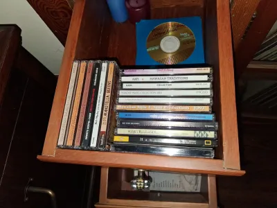 Sale Photo Thumbnail #100: Collection of music CDs in jewel cases, featuring African and Hawaiian music titles, stored inside a wooden drawer alongside a Memorex CD-R.