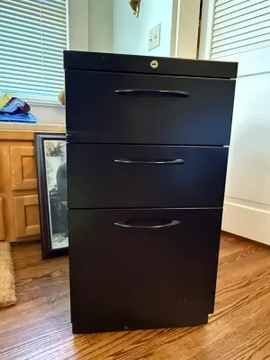 Sale Photo Thumbnail #361: Black metal three-drawer vertical filing cabinet with integrated lock and curved pull handles.