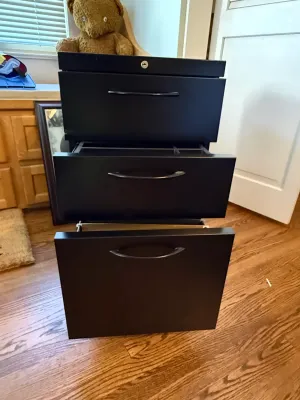 Sale Photo Thumbnail #363: Black three-drawer filing cabinet featuring curved handles and a top lock cylinder, shown with middle drawer open.
