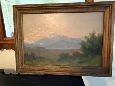Sale Photo Thumbnail #354: Framed landscape oil painting featuring mountains under a soft sky, housed in a molded wood frame with carved details.