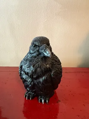 Sale Photo Thumbnail #154: Black resin or ceramic crow figurine with silver-accented beak and talons, resting on a red surface.