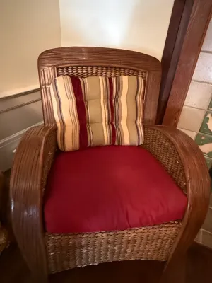Sale Photo Thumbnail #191: Vintage woven wicker and rattan armchair with broad rounded arms, featuring a red seat cushion and a striped back accent pillow.