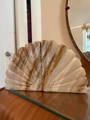 Sale Photo Thumbnail #236: Pair of carved marble or onyx fan-shaped bookends with natural brown and beige veining, shown resting on a wooden tabletop.