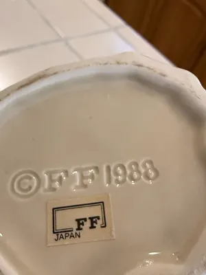 Sale Photo Thumbnail #487: Underside of a Fitz and Floyd ceramic item showing the embossed 1988 copyright mark and original paper maker's sticker.