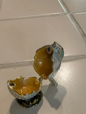 Sale Photo Thumbnail #484: Open enamelled and jeweled bird figurine trinket box, featuring a yellow glazed interior and magnetic closure.