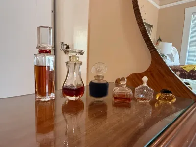 Sale Photo Thumbnail #257: Collection of vintage glass perfume bottles arranged on a mirrored wooden dresser top, including Giorgio Beverly Hills and other decorative crystal vanity bottles.