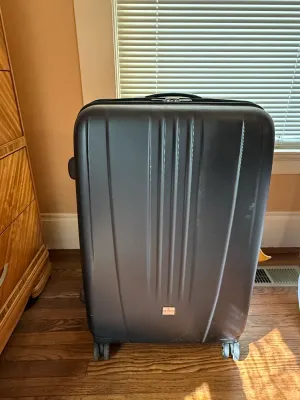 Sale Photo Thumbnail #230: Large dark grey hardshell rolling suitcase with spinner wheels, showing light scuffs from use.