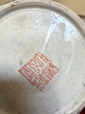 Sale Photo Thumbnail #405: Underside of a Chinese porcelain vessel displaying a red square seal mark, showing glaze imperfections and light surface wear.