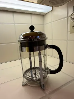 Sale Photo Thumbnail #482: Bodum French press coffee maker featuring a clear glass beaker, chrome-plated frame, and black handle.