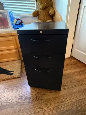 Sale Photo Thumbnail #365: Modern black metal three-drawer filing cabinet with a locking top drawer and black curved handles.