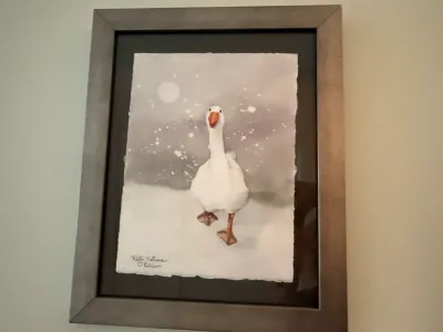 Sale Photo Thumbnail #262: Framed original watercolor painting by Kelli Folsom O'Brien depicting a white goose in a snowy landscape, float-mounted on dark matting inside a metallic silver frame.