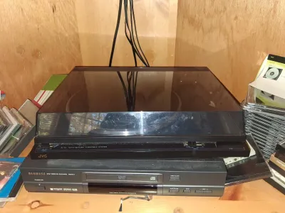 Sale Photo Thumbnail #104: Black JVC auto-return turntable stacked on a Samsung DVD/CD player, surrounded by CD jewel cases inside a wooden cabinet.