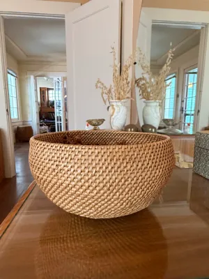 Sale Photo Thumbnail #291: Large woven rattan bowl displayed on a reflective tabletop, accompanied by decorative ceramics and dried floral arrangements in the background.