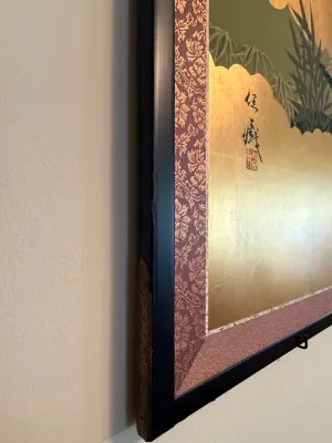 Sale Photo Thumbnail #217: Close-up detail of a framed Asian gold-leaf artwork, showing signature calligraphy, red artist seal, patterned fabric matting, and minor wear to the black frame.