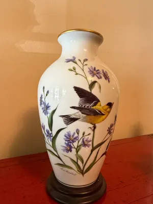 Sale Photo Thumbnail #130: Franklin Mint porcelain vase featuring a goldfinch and purple flowers by artist A.J. Rudisill, complete with a dark wooden base and gold trim.