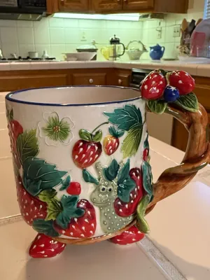 Sale Photo Thumbnail #479: Whimsical ceramic strawberry mug with relief details, a vine-shaped handle, and strawberry feet.