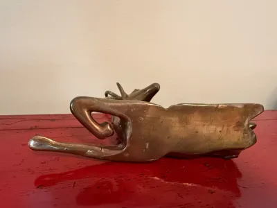 Sale Photo Thumbnail #157: Underside of a mid-century brass stylized deer figurine resting on a red surface, showing light surface scratches and aged patina.
