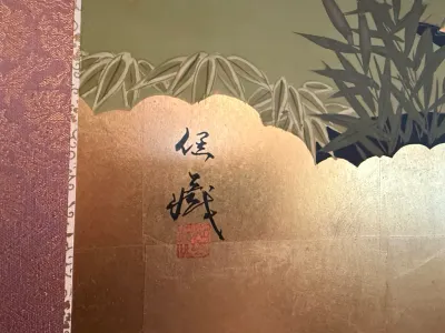 Sale Photo Thumbnail #221: Detail view of a traditional Japanese painting on a gold leaf panel featuring bamboo foliage, calligraphy signature, and red artist seal.