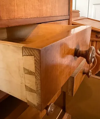 Sale Photo Thumbnail #306: Close-up of a vintage wood desk drawer showing hand-cut dovetail joinery and turned wooden knobs.