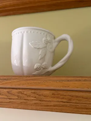 Sale Photo Thumbnail #456: White ceramic mug featuring embossed berry and leaf details with a beaded rim and twisted handle.