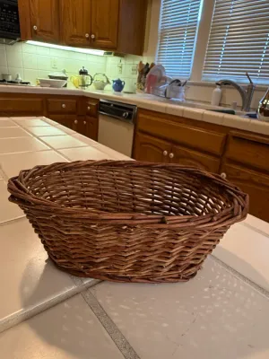 Sale Photo Thumbnail #446: Handwoven oval wicker basket sitting on a tiled countertop, featuring a natural dark brown finish and thick braided rim.