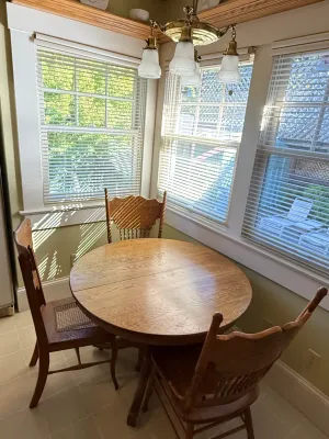 Sale Photo Thumbnail #462: Round wooden pedestal dining table paired with three carved oak side chairs, accompanied by a suspended brass chandelier light fixture.