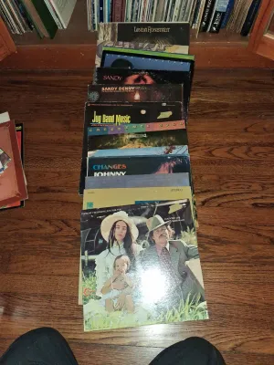 Sale Photo Thumbnail #98: A stack of vintage vinyl LP record albums on a wood floor, featuring artists such as Country Joe McDonald, Creedence Clearwater Revival, Sandy Denny, and Linda Ronstadt.