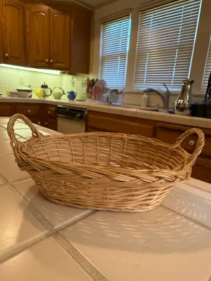 Sale Photo Thumbnail #475: Oval wicker serving basket with two looped side handles, shown resting on a tiled countertop.