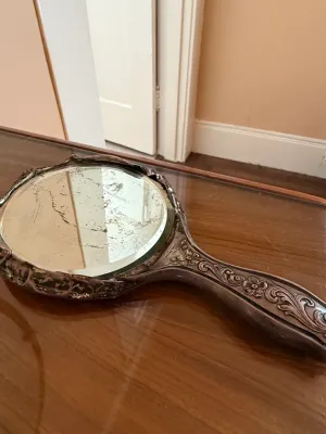 Sale Photo Thumbnail #247: Vintage sterling silver hand mirror with an ornate floral handle, featuring age-related desilvering on the glass.