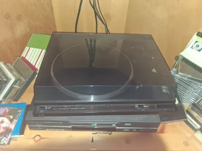 Sale Photo Thumbnail #101: Black JVC auto-return turntable system stacked on top of a Samsung DVD/Video CD/CD player, surrounded by CD cases.