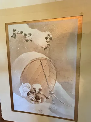 Sale Photo Thumbnail #301: Japanese artwork print depicting puppies in a snowy scene near a woven basket shelter, mounted on a cream-colored board with metallic border accents.