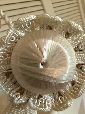 Sale Photo Thumbnail #372: Close-up view of an ornate off-white decorative curtain tieback, featuring a woven silk dome surrounded by intricate passementerie gimp trim.
