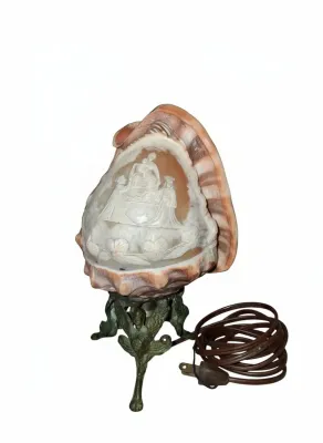 Sale Photo Thumbnail #74: Vintage carved conch shell cameo night lamp featuring a religious scene, mounted on an ornate bronze-toned tripod base.