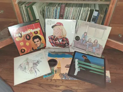 Sale Photo Thumbnail #119: Collection of vintage vinyl records displayed in front of a wooden record cabinet shelf, featuring titles by Elvis Presley, Crosby, Stills & Nash, and Frank Wakefield.