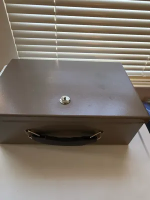 Sale Photo Thumbnail #383: Portable metal lockbox with keyhole mechanism and black carrying handle.