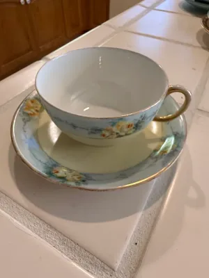 Sale Photo Thumbnail #460: Vintage porcelain teacup and saucer set with a light blue and pale yellow ground, hand-painted yellow roses, and gilded trim.