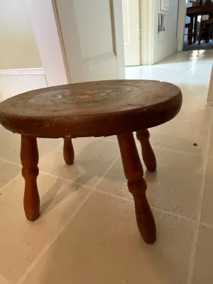 Sale Photo Thumbnail #425: Vintage small round wooden stool with turned legs and faint hand-painted details on top, showing age-appropriate surface wear.