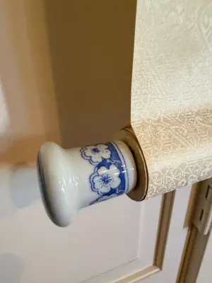 Sale Photo Thumbnail #374: Detail view of an Asian hanging scroll with patterned silk fabric and a blue-and-white porcelain roller end.