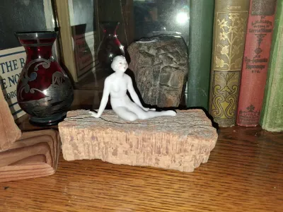 Sale Photo Thumbnail #69: Art Deco style porcelain bathing beauty figurine resting on a cork base, displayed alongside a silver overlay ruby glass vase and vintage books.
