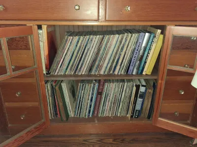 Sale Photo Thumbnail #99: Collection of vinyl LP records and art books stored inside a wooden cabinet with glass-paneled doors.