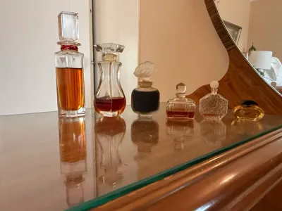Sale Photo Thumbnail #256: Collection of vintage glass perfume bottles arranged on a wooden vanity top, including a Giorgio Beverly Hills bottle and various decorative stoppers.