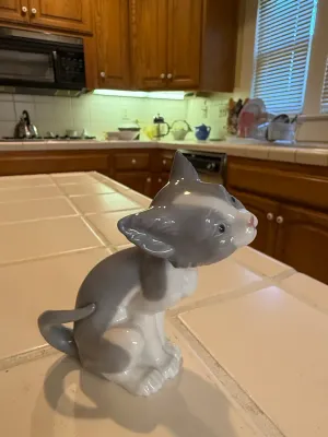 Sale Photo Thumbnail #500: Glazed porcelain cat figurine, depicting a sitting grey and white kitten scratching its ear, shown with a chipped left ear.