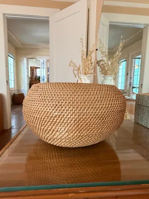 Sale Photo Thumbnail #290: Large rounded woven rattan or wicker decorative bowl sitting on a glass-topped wooden table.