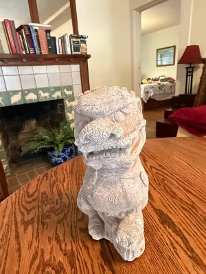 Sale Photo Thumbnail #174: Hand-carved stone foo dog statue sitting on a wooden tabletop, showing a textured, weathered finish.