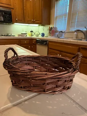 Sale Photo Thumbnail #447: Oval dark brown wicker basket with twisted side handles, set on a tiled kitchen counter.