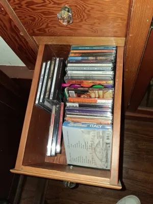 Sale Photo Thumbnail #97: Collection of compact discs in jewel cases, featuring various musical artists and world music compilations, stored inside a wooden furniture drawer.