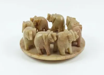 Sale Photo Thumbnail #61: Hand-carved soapstone or marble elephant processional sculpture on a round base, featuring a circle of small elephants.