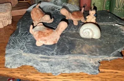 Sale Photo Thumbnail #39: Collection of miniature items, including three clay turtle figurines, a small wooden angel ornament, and a seashell, displayed on a slate slab with plant impressions.