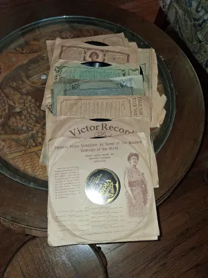 Sale Photo Thumbnail #125: Collection of vintage 78 RPM Victor shellac records in original paper sleeves, displayed on a glass-top table.